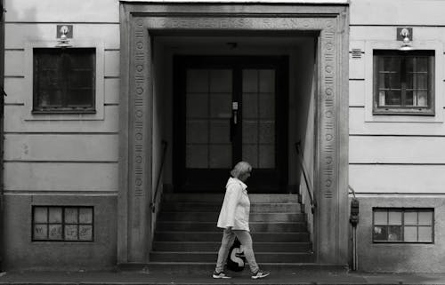 Grayscale Photo of a Woman Walking near a Door