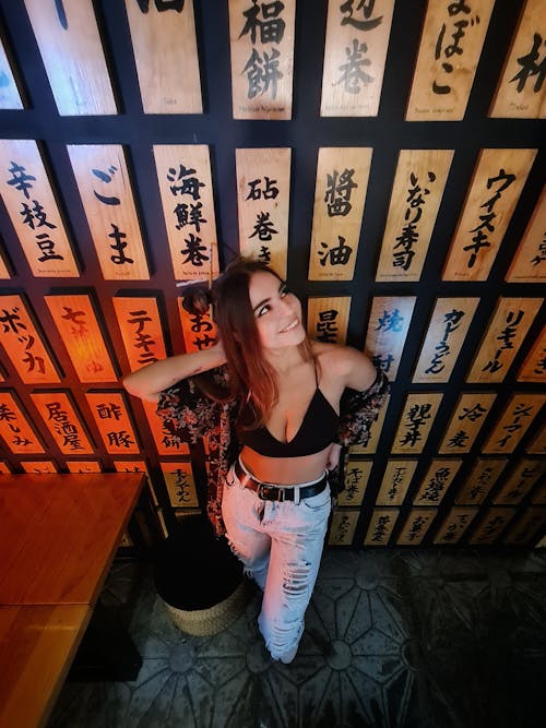 Alluring Woman in Black Brassiere and Tattered Jeans leaning on a Wall with Japanese Wooden Ornaments 