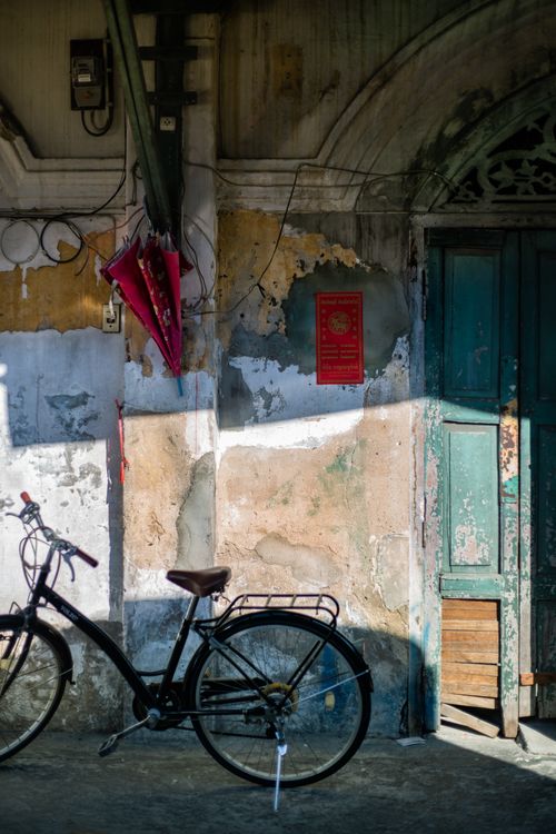 Free Black bicycle parked by an old, weathered wall with peeling paint and a rustic door. Stock Photo