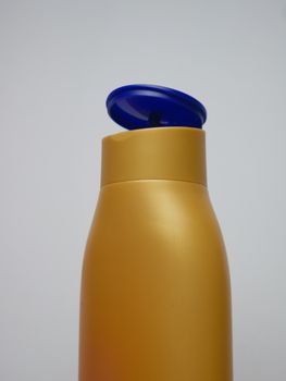 Close-up of a gold plastic bottle with a blue flip cap against a neutral background.