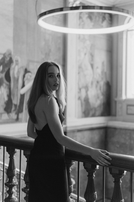 A woman in an elegant black dress looks back in a monochrome artistic setting.