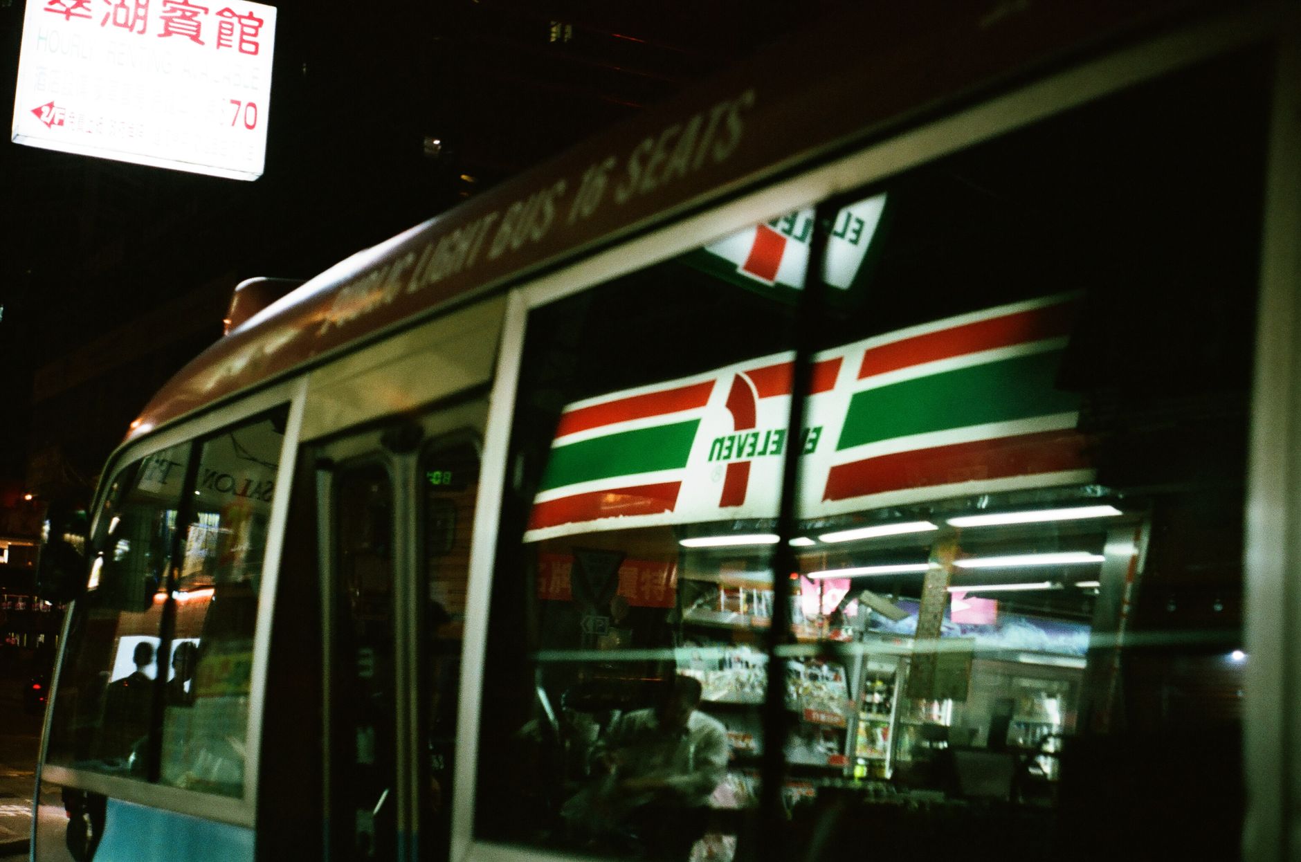 Night scene in Kowloon with a bus reflecting signage and street lights.