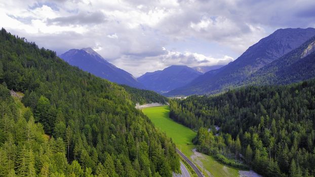 Scenic view of an Austrian mountain valley with lush green forest and distant peaks under a cloudy sky.