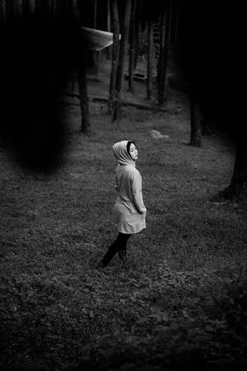 Grayscale Photo of a Woman in a Jacket Standing on Grass