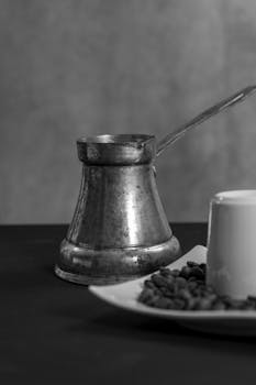 Monochrome still life featuring a coffee pot, cup, and plate of coffee beans.