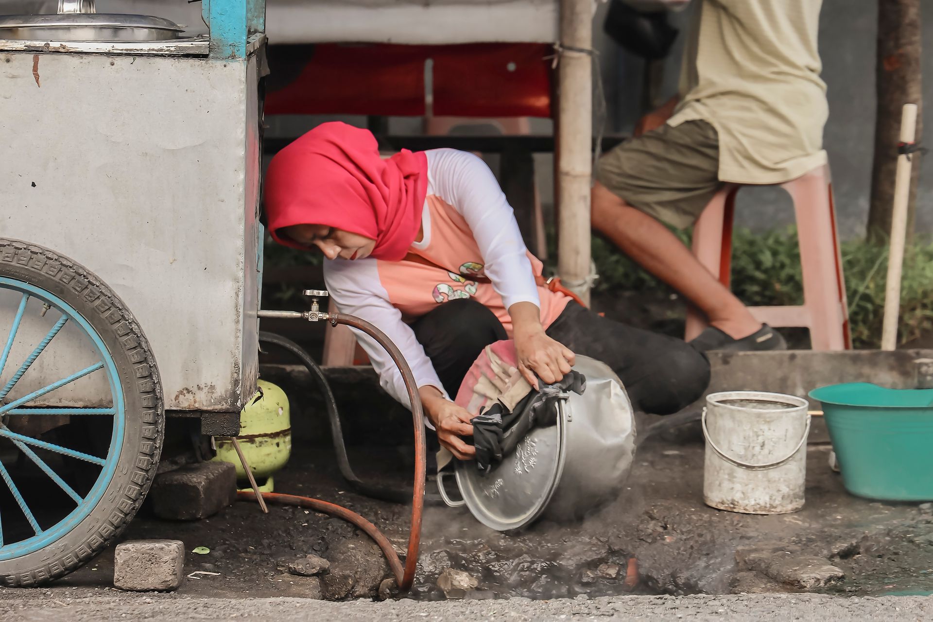 A street vendor in Yogyakarta washing a cooking pot outdoors. Authentic local scene.