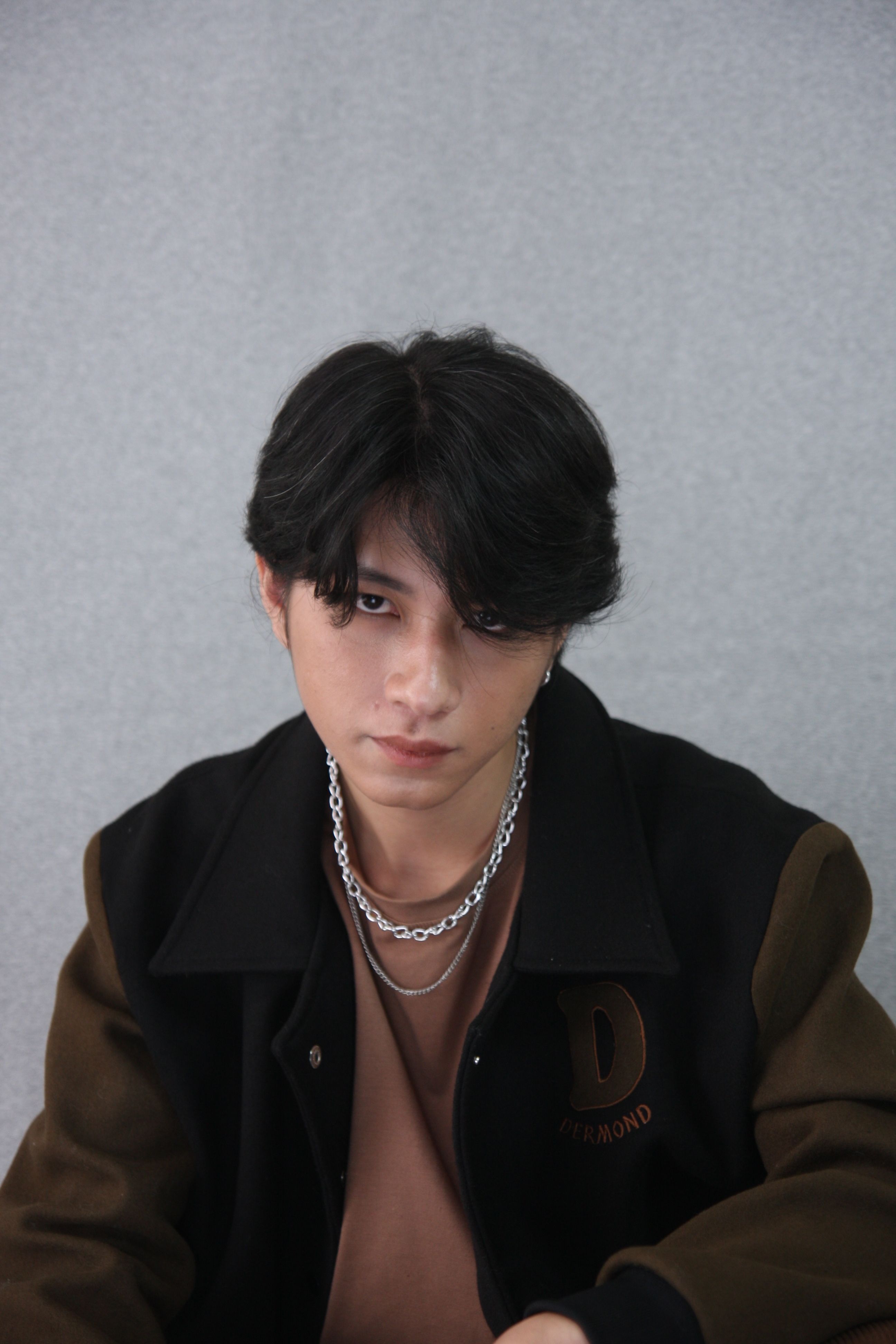 Young man with a serious gaze wearing a jacket and silver necklaces.
