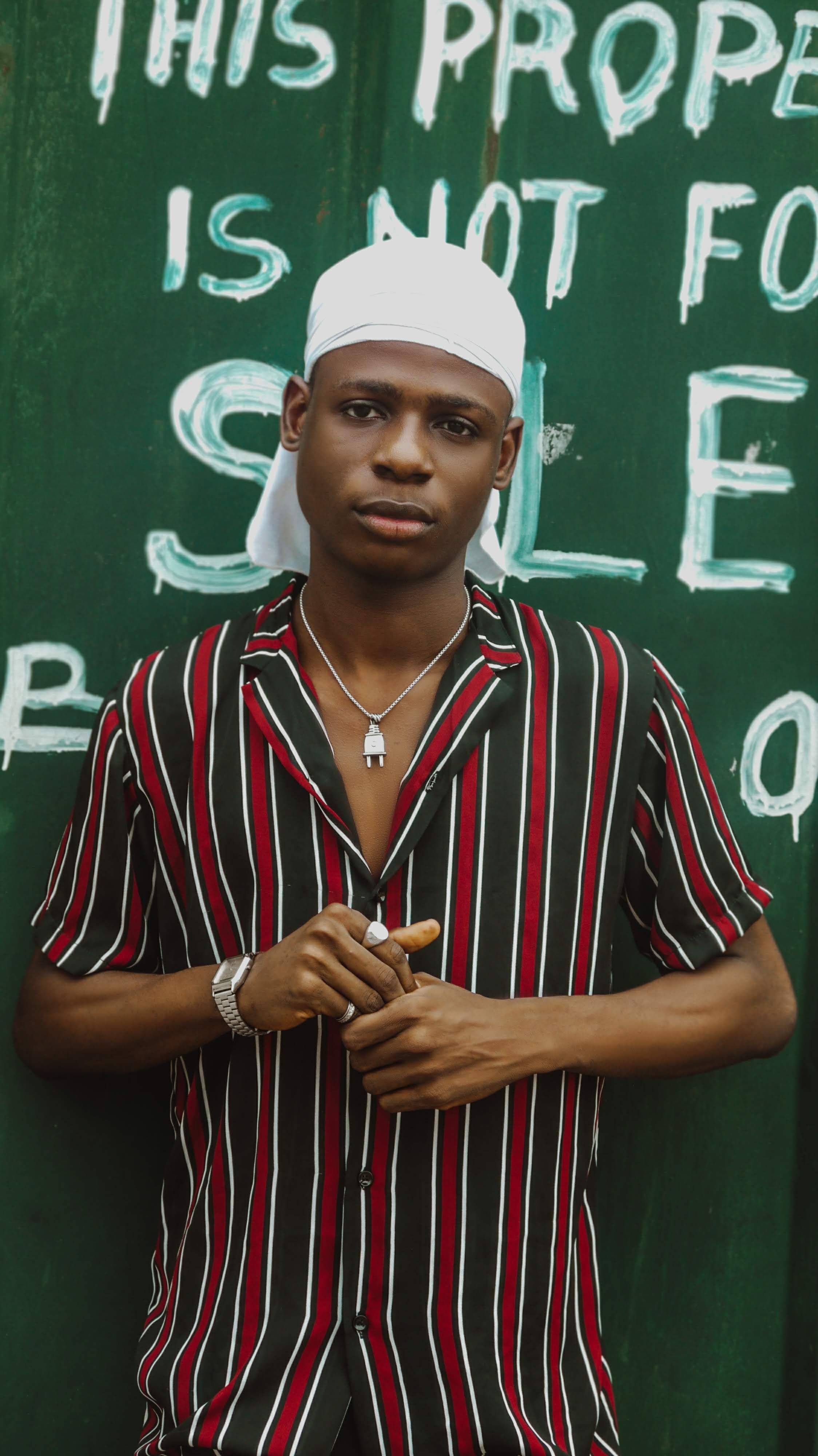 Portrait of a young man wearing a striped shirt, standing against a green urban graffiti wall.