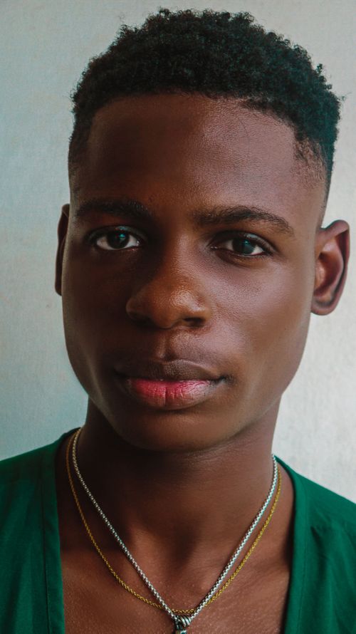 Free Close-up portrait of a serious young man wearing necklaces, showcasing natural beauty and style. Stock Photo