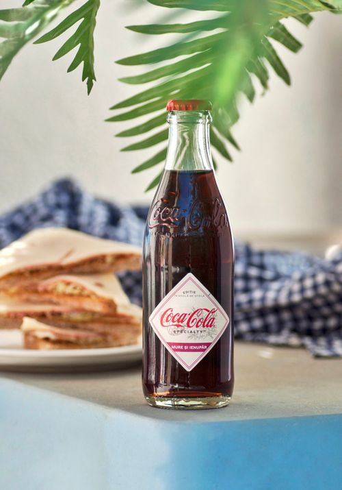 Free Classic Coca Cola bottle placed on a table with sandwiches and foliage in a sunny setting. Stock Photo