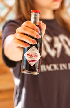 Close-up of a woman in a T-shirt holding a classic Coca-Cola bottle outdoors, highlighting summer refreshment.