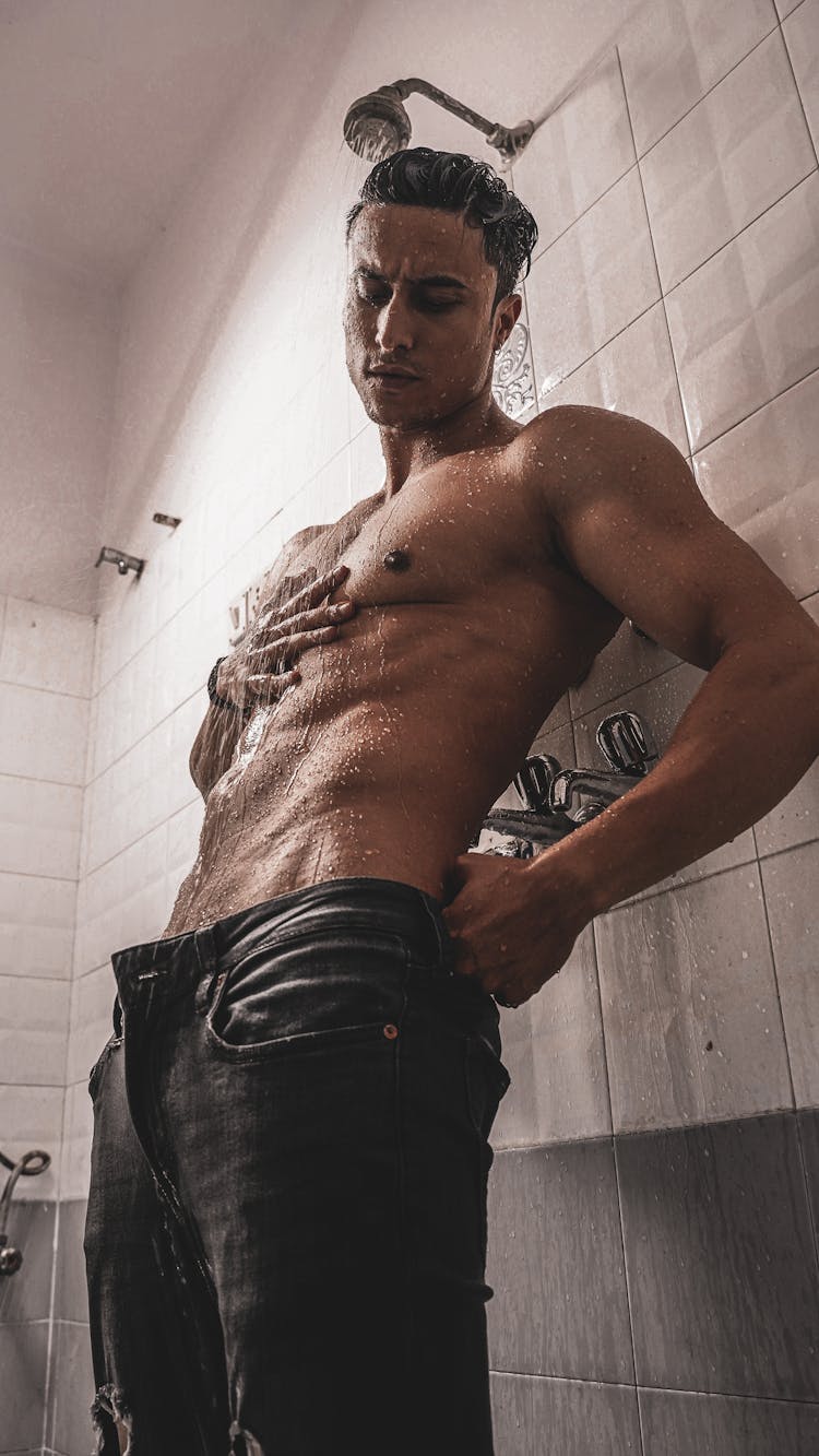 A Shirtless Man Showering In The Bathroom 