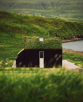 A tranquil Faeröer house with a green roof nestled in lush hills by the sea.