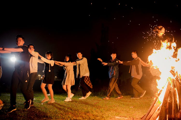 A Group Of Friends Circling A Campfire