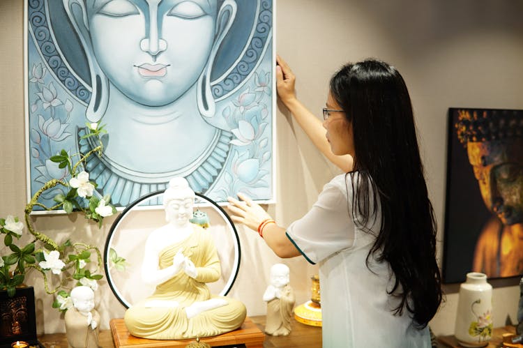 A Woman Arranging A Framed Buddha Painting