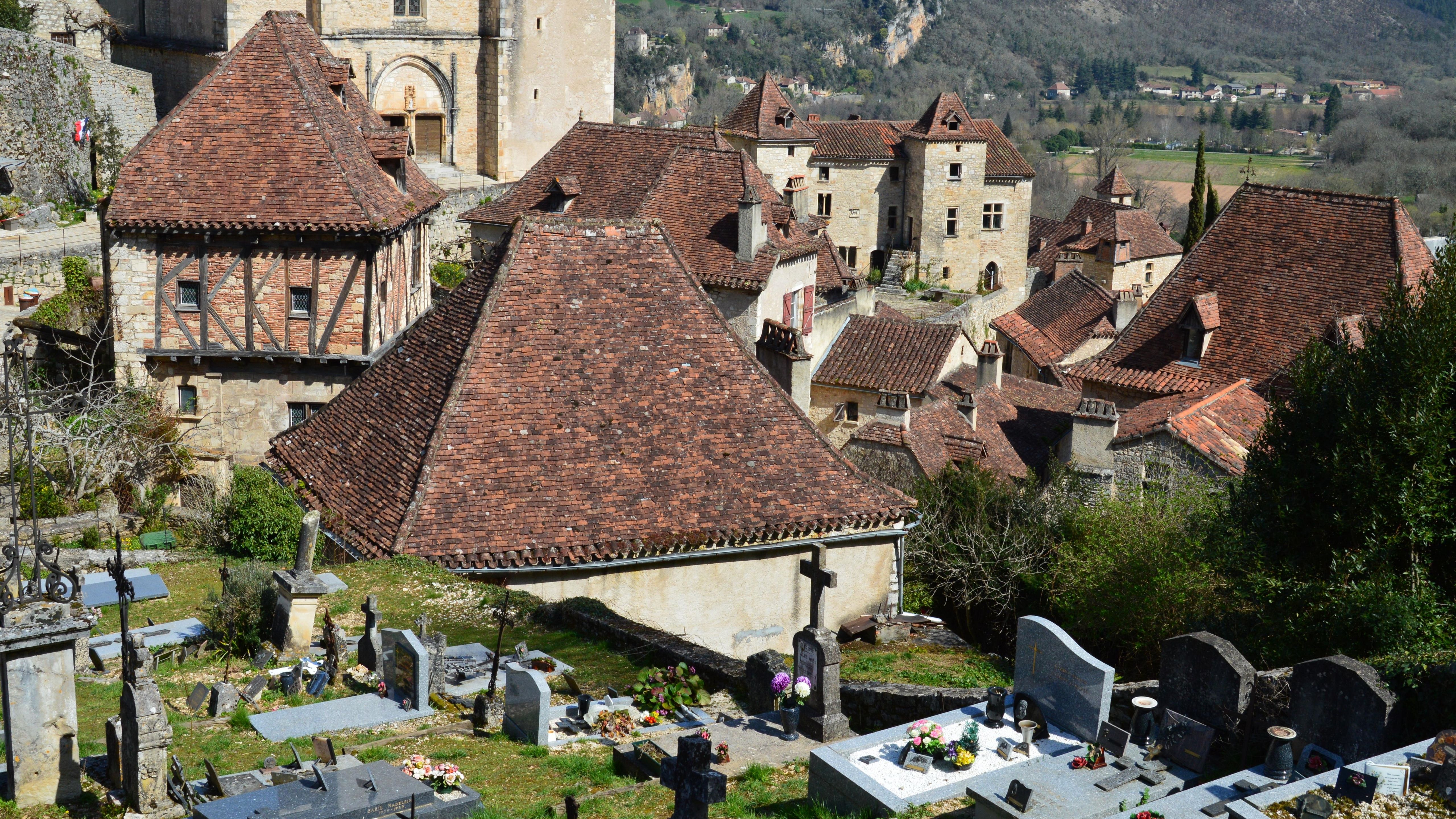 Aerial view of a medieval village with rustic rooftops and an adjacent cemetery.