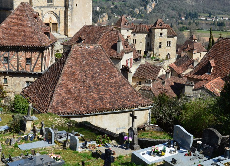 Aerial view of a medieval village with rustic rooftops and an adjacent cemetery.