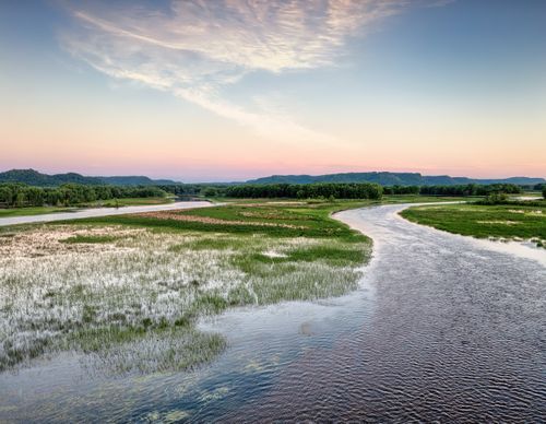 Free A peaceful sunrise over a river landscape in Plainview, MN, with lush greenery and calm waters. Stock Photo