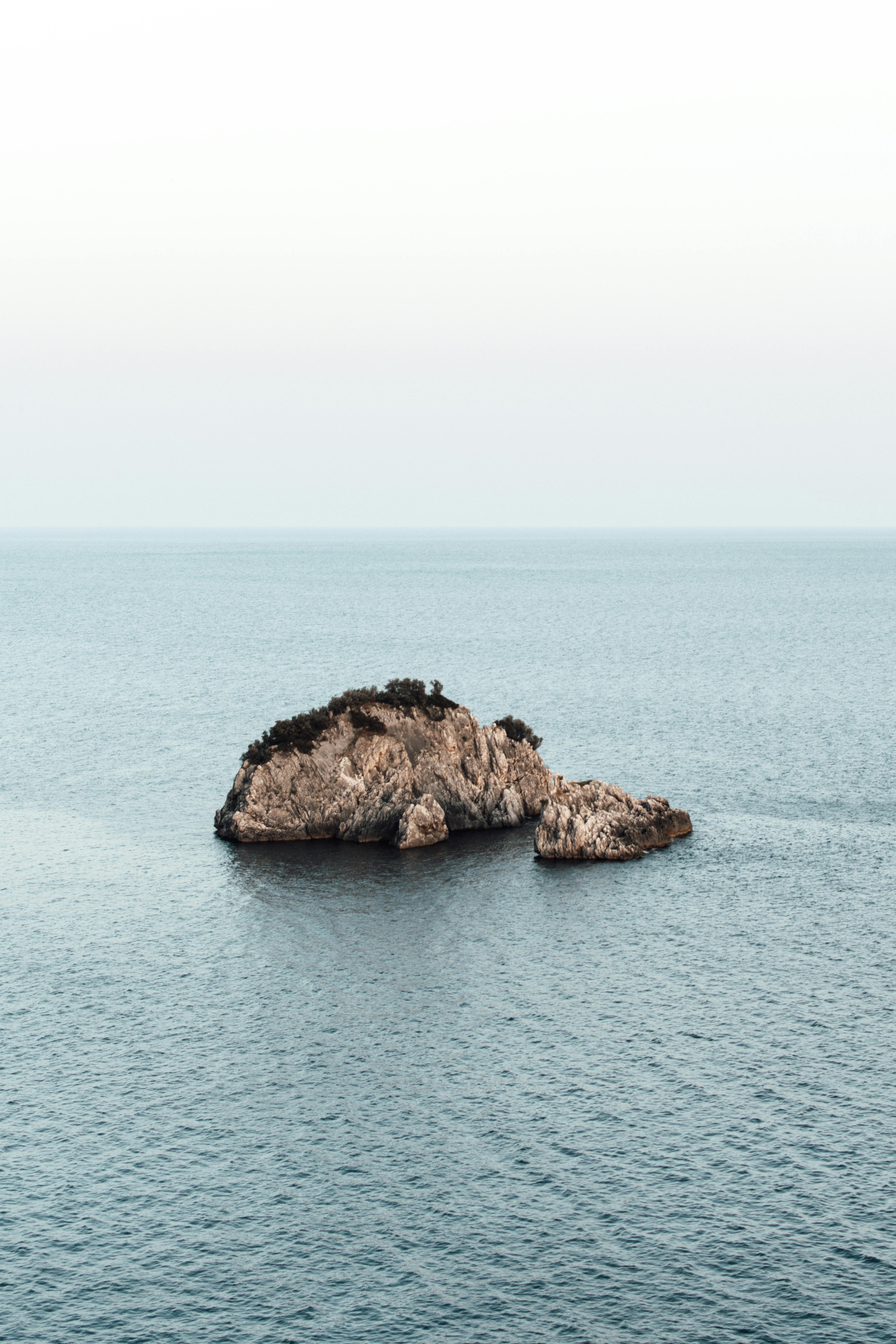 A peaceful aerial shot of a solitary rock formation surrounded by calm sea waters.