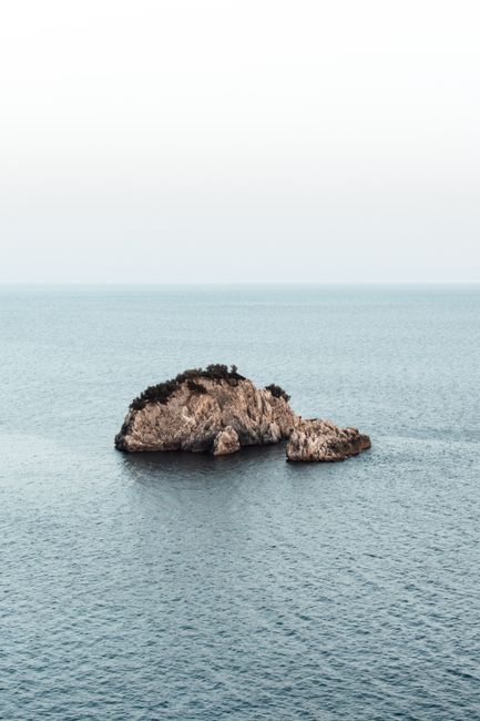 A peaceful aerial shot of a solitary rock formation surrounded by calm sea waters.