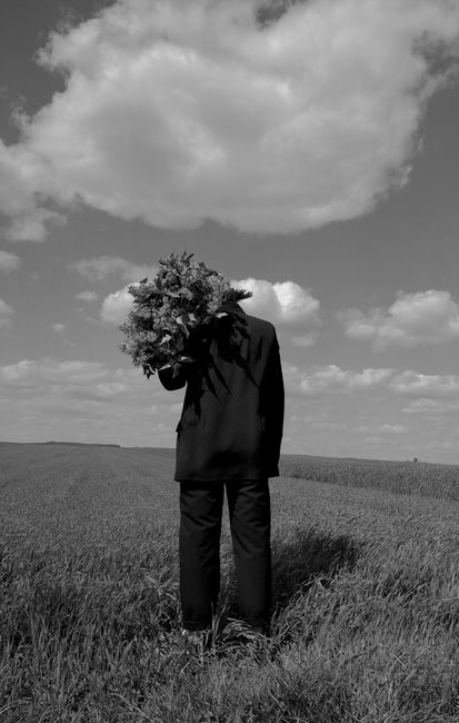 Black and white photo of a man in a suit holding flowers in a vast open field.