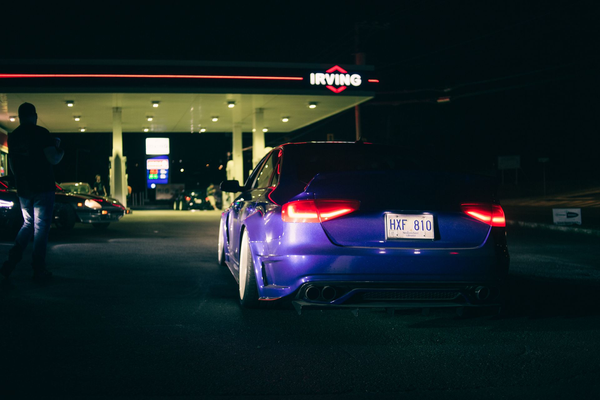 Blue Audi S4 parked near a gas station at night with bright lights and dramatic shadows.