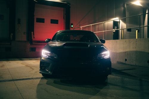Free Front view of a sleek black sports car with headlights on at night. Stock Photo