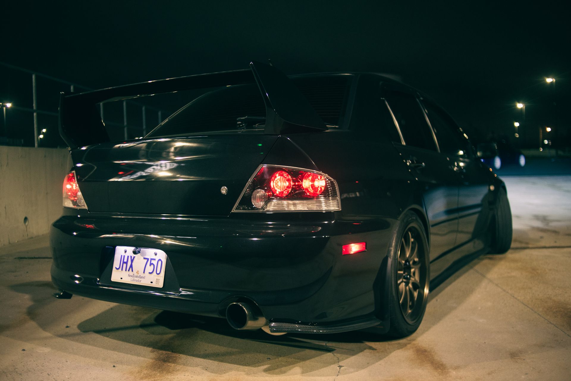 A sleek Mitsubishi Lancer Evolution parked outdoors at night, showcasing its sporty design and bold tail lights.