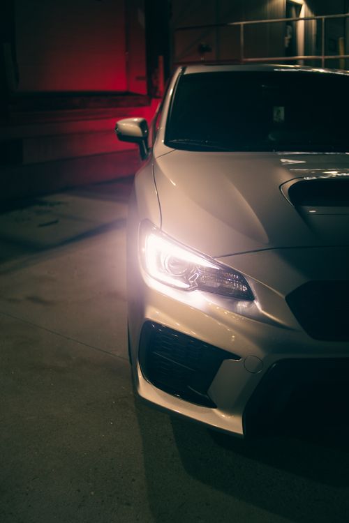Free Stylish silver car parked at night, headlights on, creating a modern urban vibe. Stock Photo