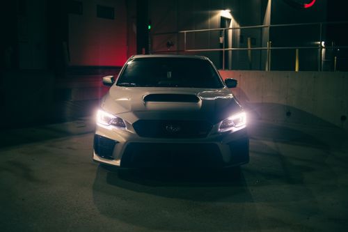 Free Front view of a sports car in a dimly lit garage, showcasing sleek design and headlights. Stock Photo