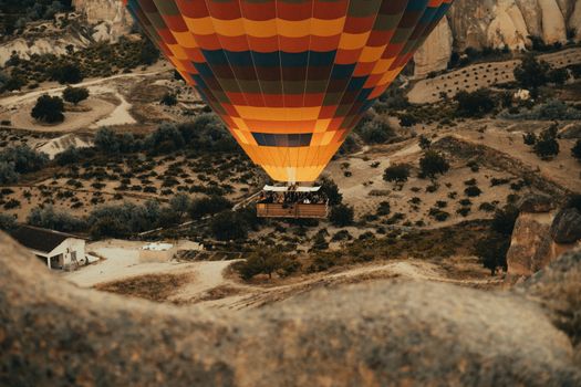 Vibrant hot air balloon flying over Cappadocia's unique terrain, captured from above.
