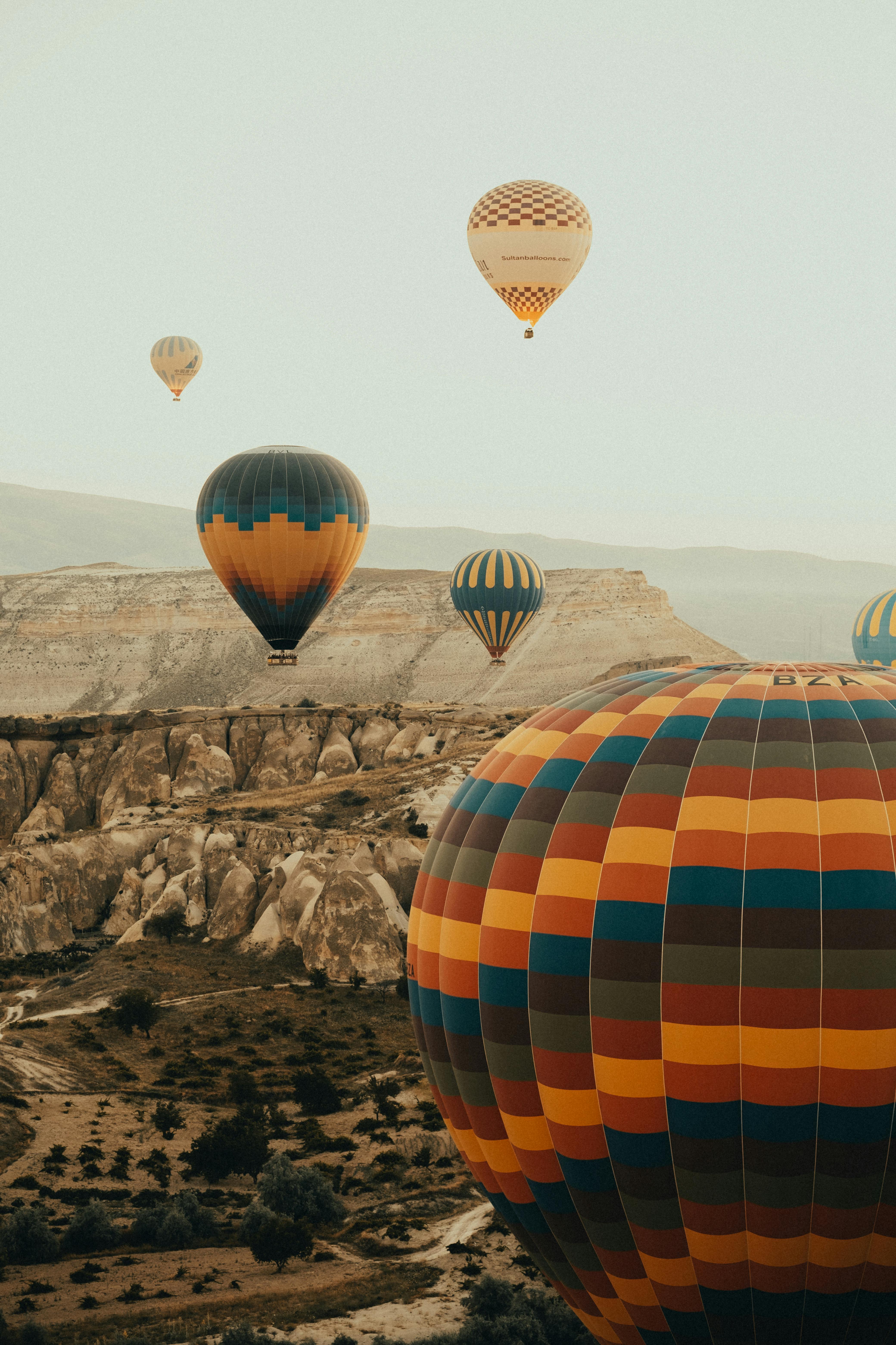 Colorful hot air balloons flying over Cappadocia's rocky formations during a clear summer day.