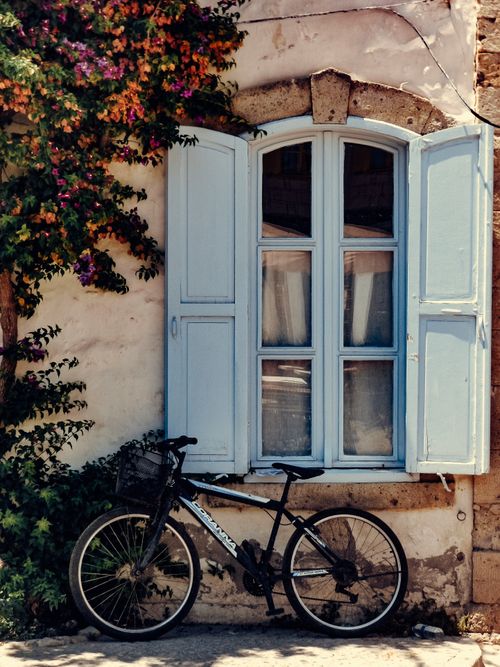Free A vintage bicycle leans against a wall adorned with vibrant flowers and a rustic window frame. Stock Photo