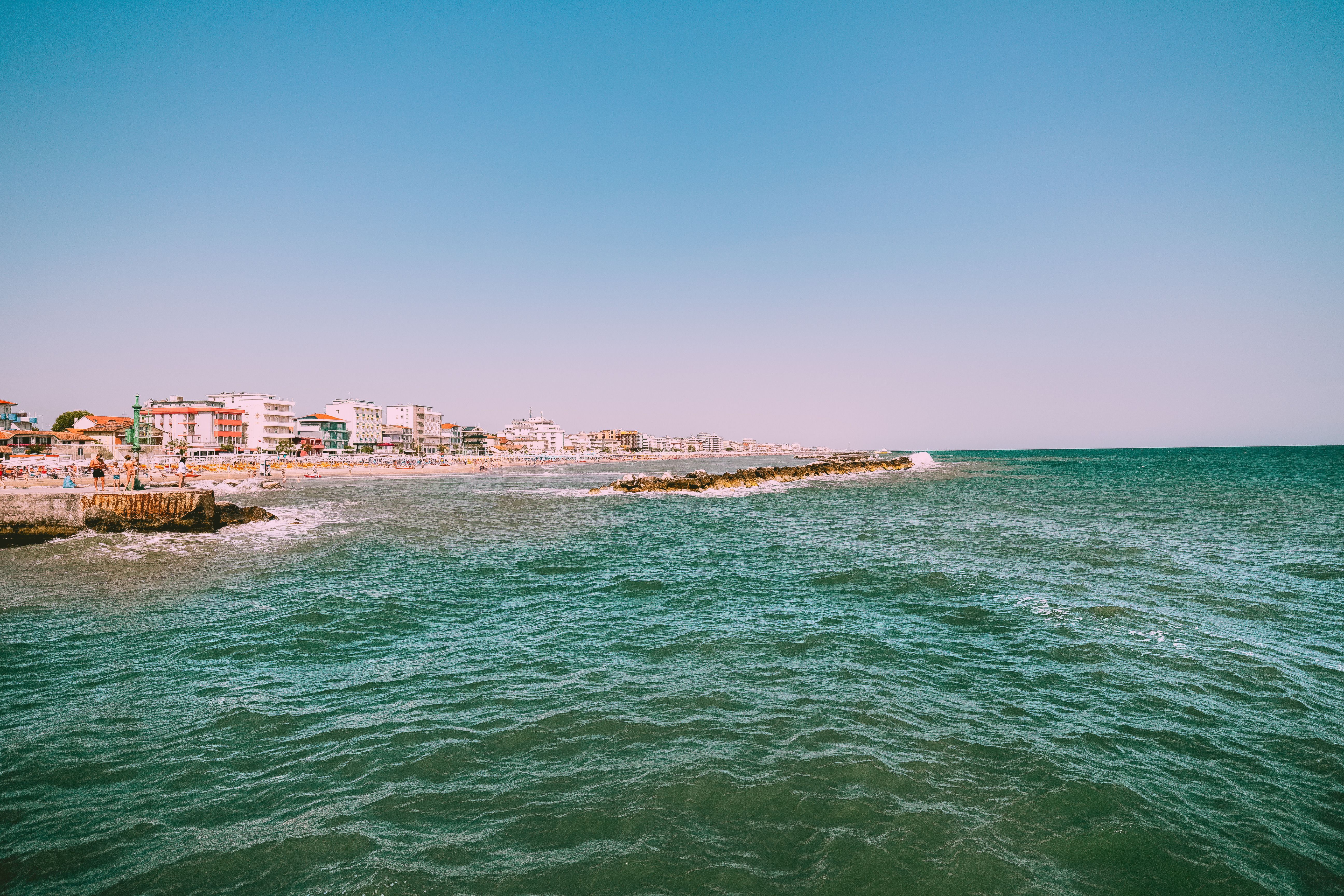 Vibrant coastal scene with blue sky, ocean waves, and seaside buildings on a sunny day.