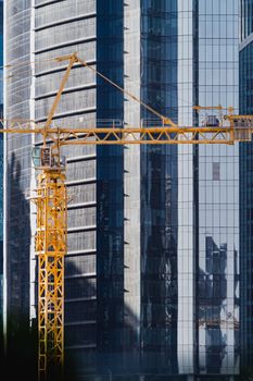 A vertical shot of a construction crane against modern skyscrapers in a city environment.