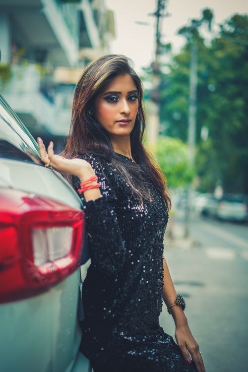 Free Indian woman elegantly posing next to a car on a street in Delhi, India. Stock Photo