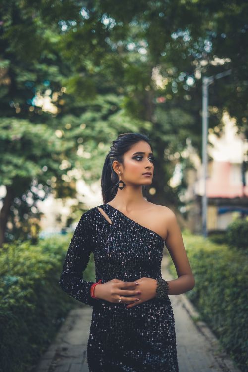 Free A fashionable Indian woman in a one-shoulder sequin dress standing outdoors, exuding elegance. Stock Photo