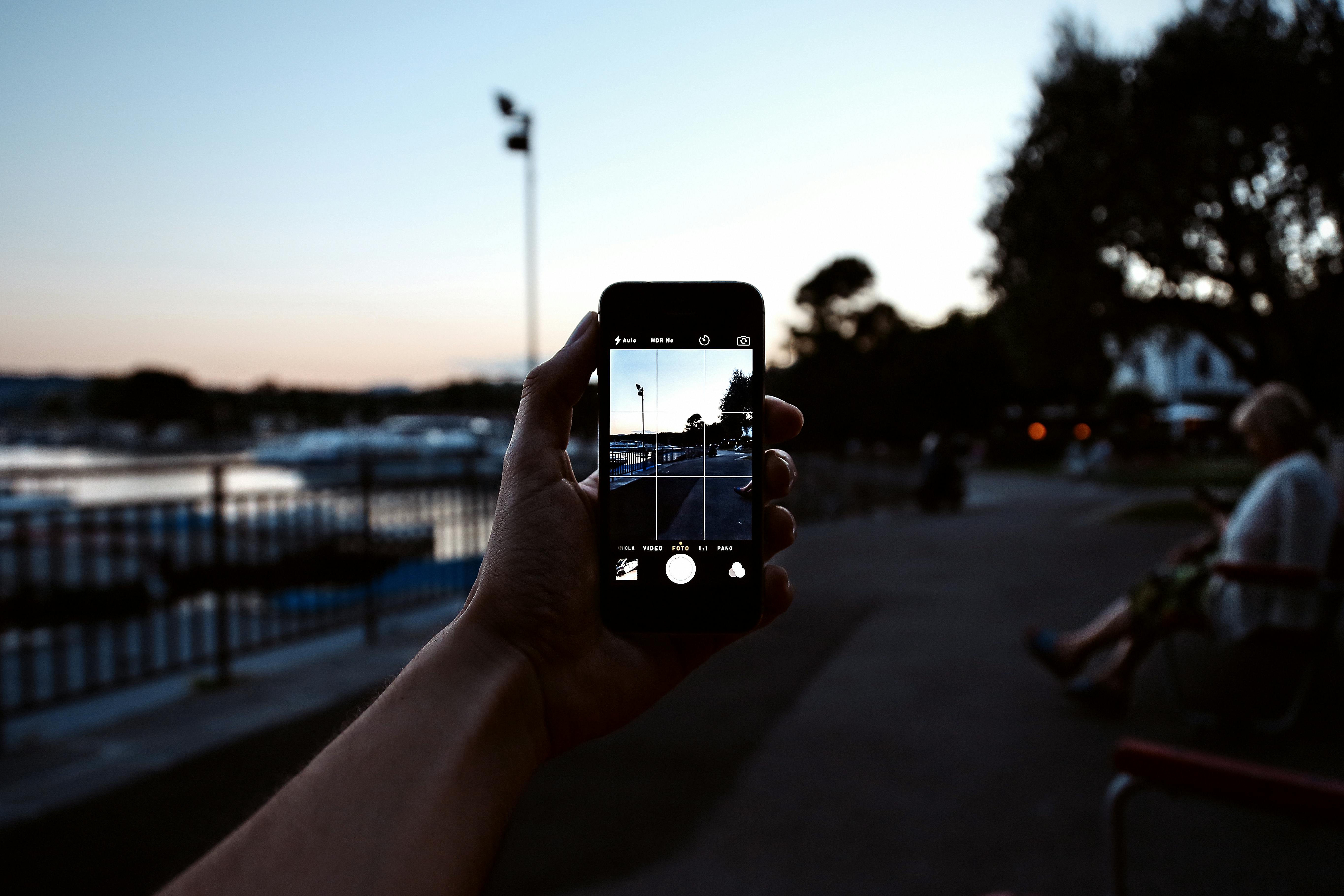 Free A hand holding a smartphone captures a serene evening park scene. Stock Photo
