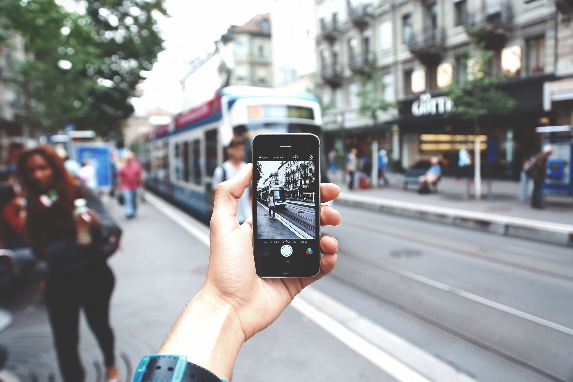 A person's hand capturing a city street and tram using a smartphone camera.