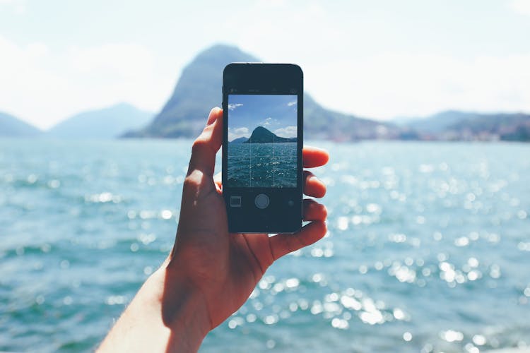 Hand Holding Cellphone Taking Photo Of Ocean