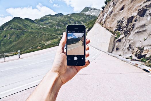 Hand holding smartphone captures winding mountain road scene.