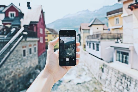 A hand holding a smartphone capturing a scenic mountain village view.