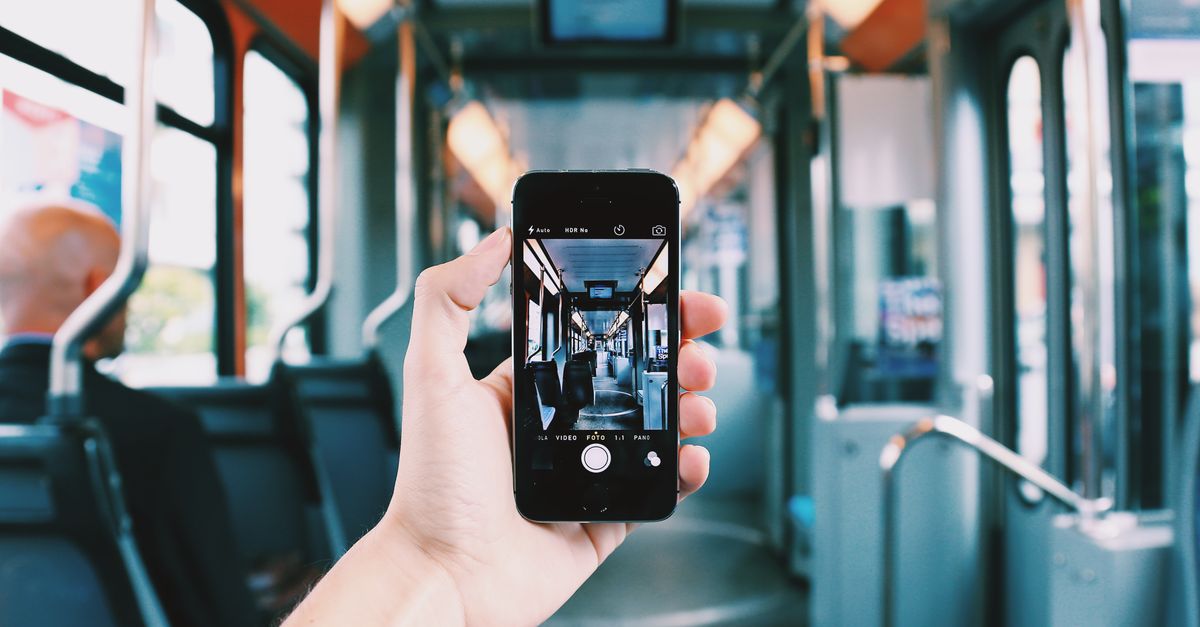 A hand holds a smartphone, capturing the interior of a train, creating a unique visual perspective.