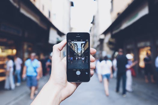 A smartphone held in hand captures a bustling city street scene.
