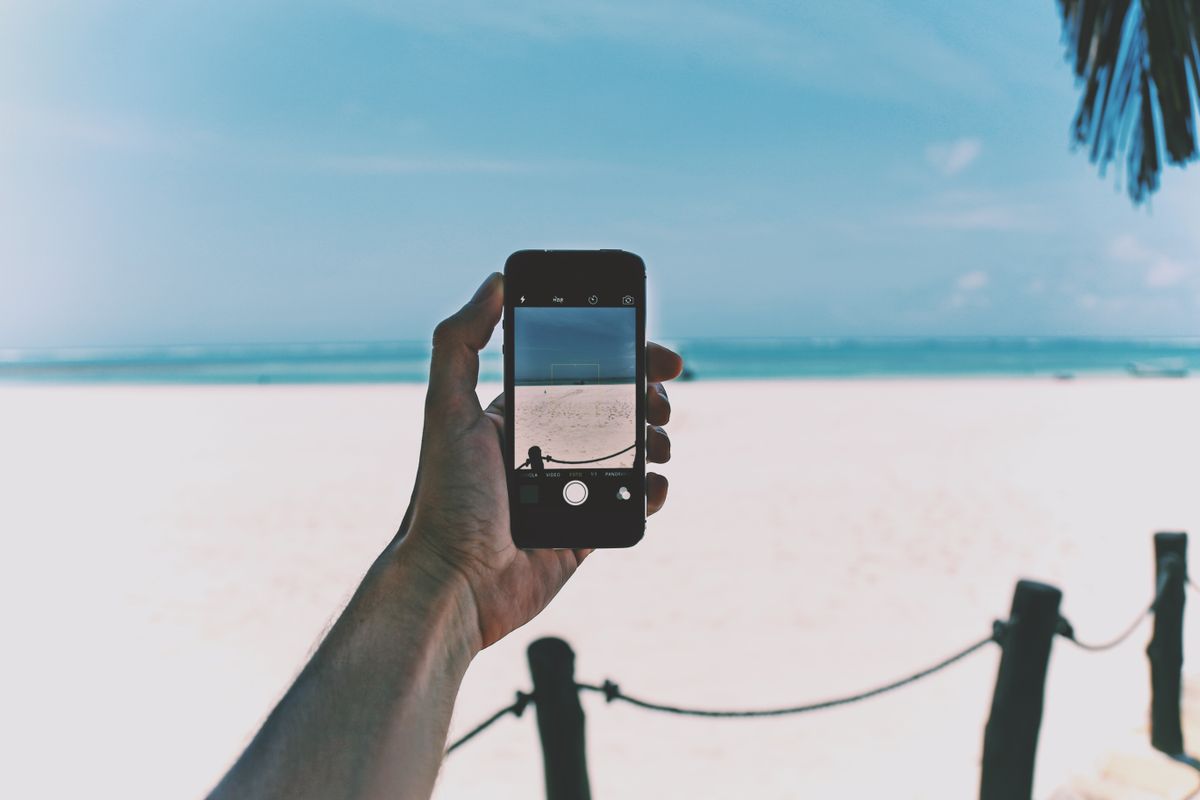 Akıllı telefon tutan bir kişi tropikal plajda oturuyor