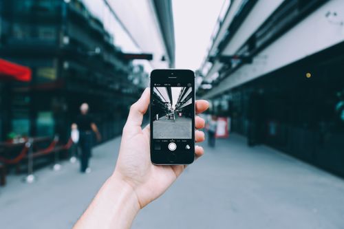 Free Close-up of a hand holding a smartphone capturing an urban street view. Modern digital photography concept. Stock Photo