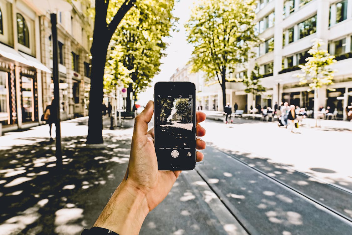 Free Hand Holding Cellphone Taking Picture on City Street Stock Photo