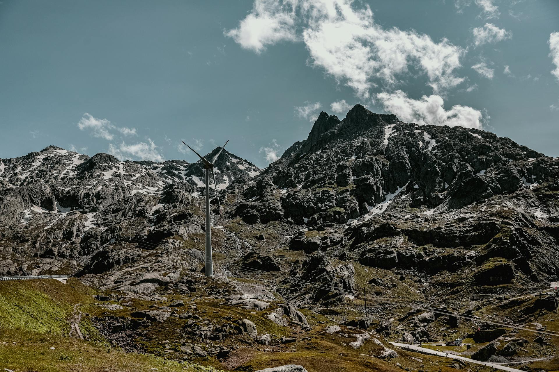 A wind turbine stands amid rugged mountains on a sunny day.