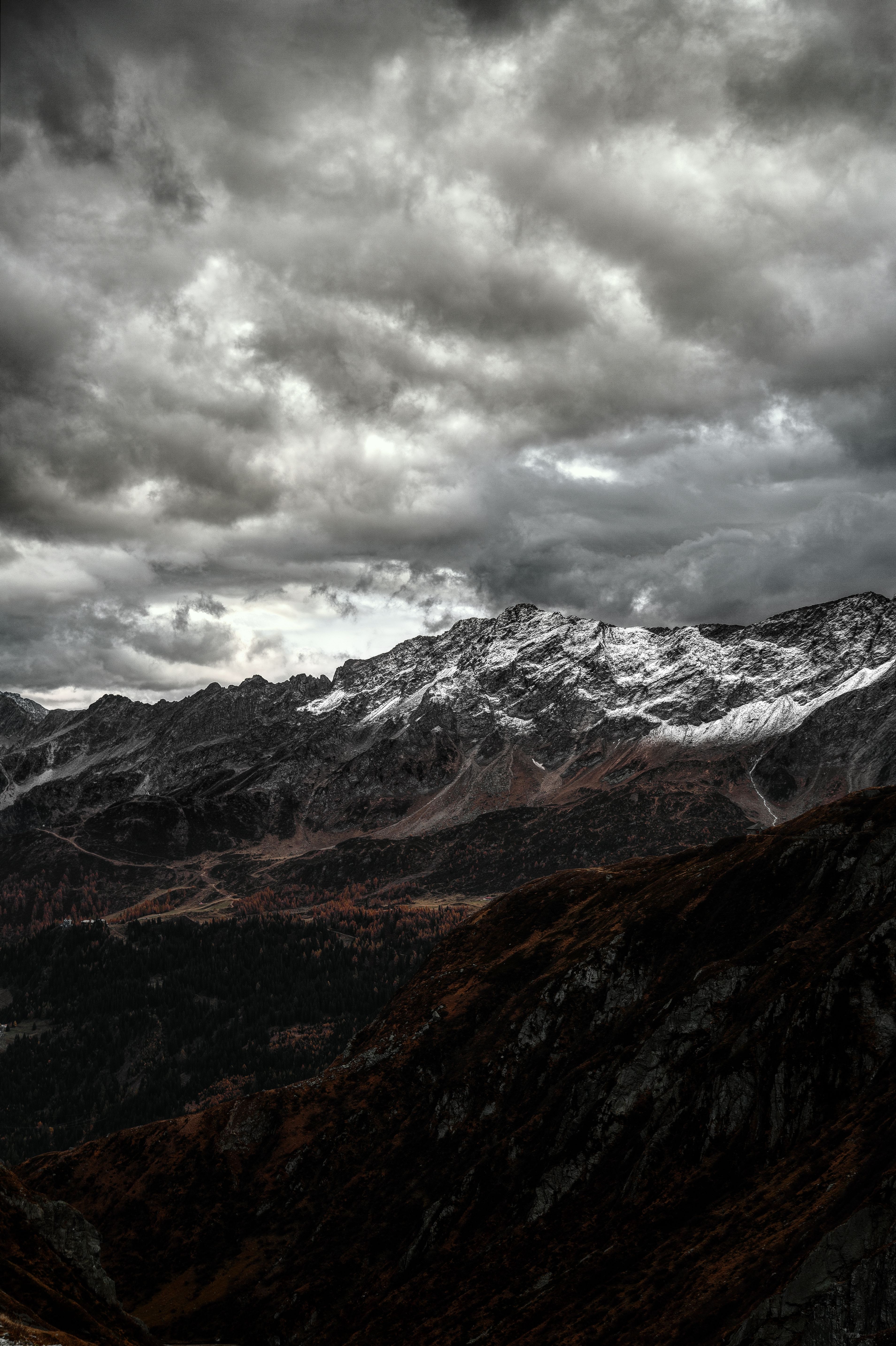 Moody landscape of the Swiss Alps with dramatic clouds, snowy peaks, and rugged terrain.