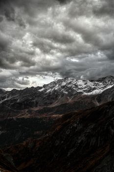 Moody landscape of the Swiss Alps with dramatic clouds, snowy peaks, and rugged terrain.